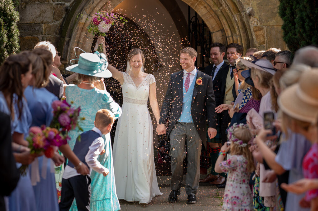 Wedding guests throwing confetti over bride and groom outside church