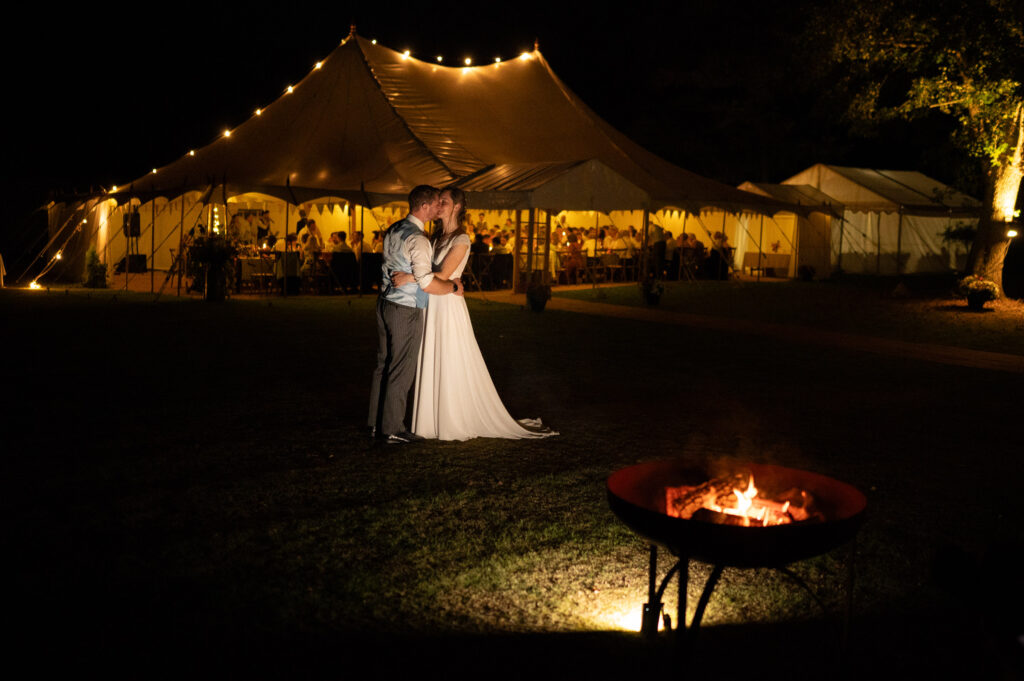 Bride and groom ar night near fire pit and marquee